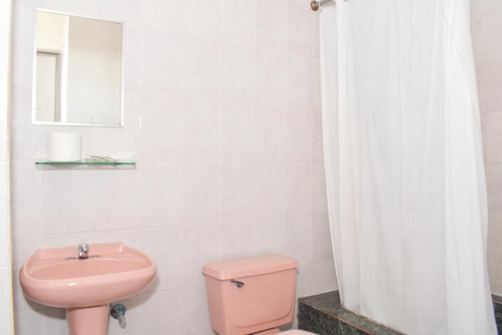 A bathroom with a pink sink, a toilet, a glass shelf, and a white shower curtain.