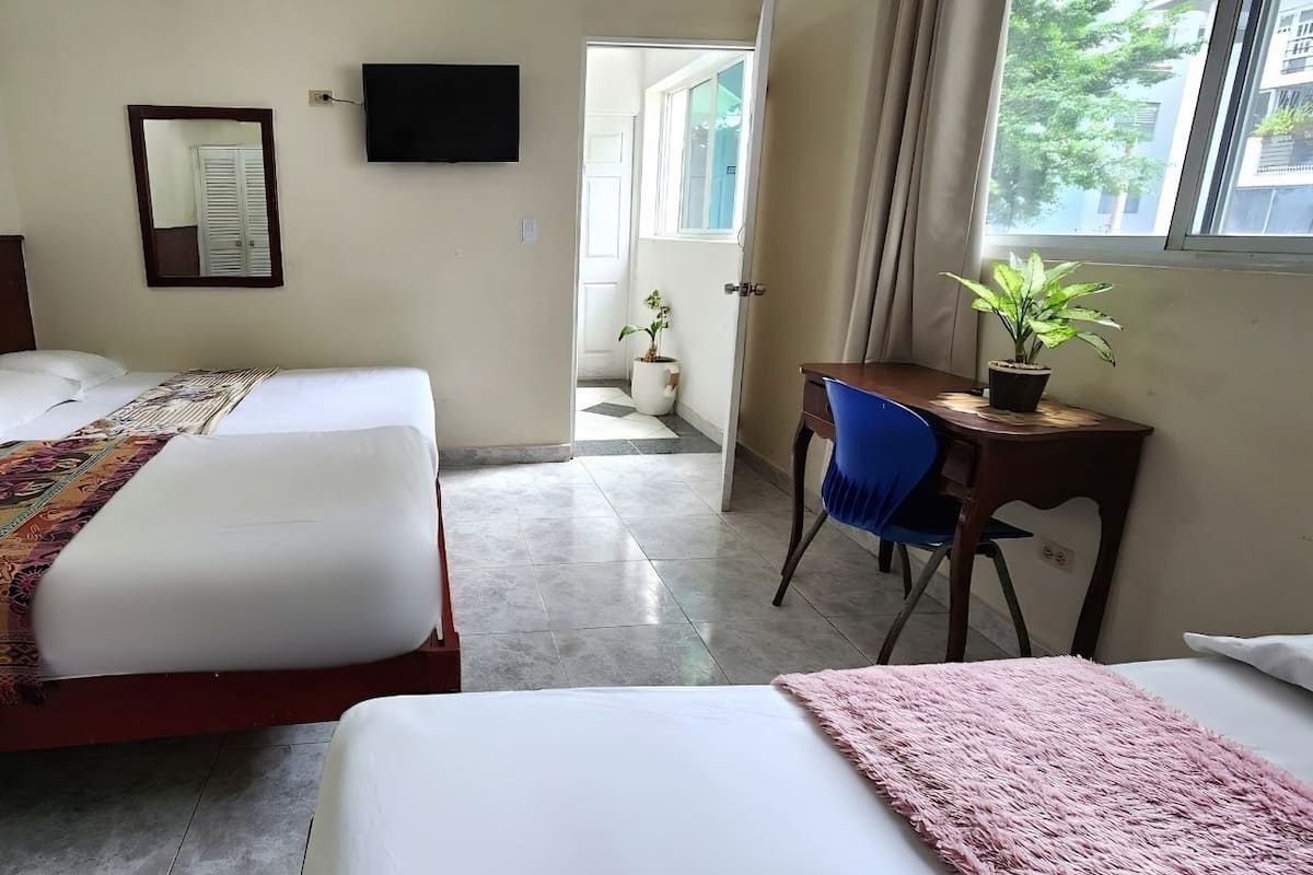 Une chambre d’hôtel avec deux lits, un bureau, une chaise, une télévision et une fenêtre donnant sur des immeubles.