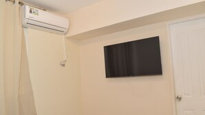 A bathroom with a shower curtain, a mounted air conditioner, and a flat-screen TV on the wall.