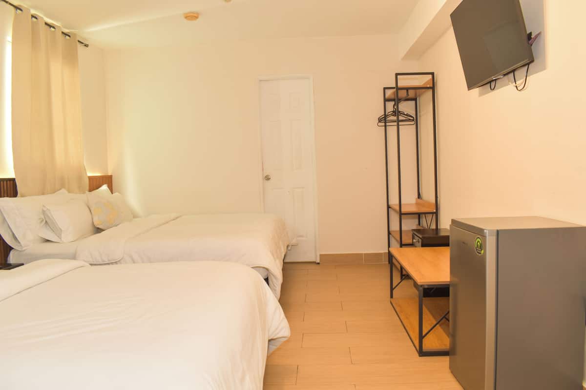 Une chambre d’hôtel avec deux lits, un plancher en bois, une armoire, une télévision et une porte.