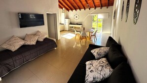 Een moderne woonkamer met een donkere bank, een eethoek met een tafel en stoelen, en een keuken op de achtergrond.