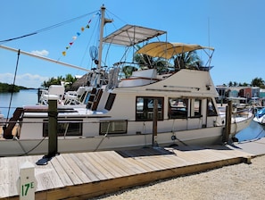 A boat docked at a pier with a wooden deck, a covered area with a canopy, and a small cabin with windows. - Southern Cross 40 ft 1977 Marine Trader | Free Kayaks (Monroe County)