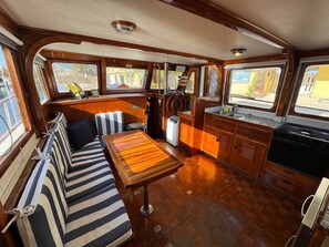 A boat interior with a dining area, a kitchen, and a seating area with striped cushions. - Southern Cross 40 ft 1977 Marine Trader | Free Kayaks (Monroe County)