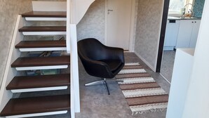 A modern interior with a staircase, a black chair, and a kitchen area. - Cozy Country Cottage in Scenic Location near Mönsterås | SE05055 (Mönsterås)