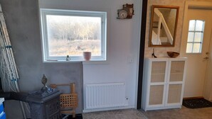 A room with a large window, a radiator, a wooden cabinet, a mirror, and a door. - Cozy Country Cottage in Scenic Location near Mönsterås | SE05055 (Mönsterås)