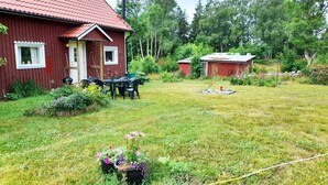 A red wooden house with a tiled roof, a garden with a table and chairs, and a small pond. - Cozy Country Cottage in Scenic Location near Mönsterås | SE05055 (Mönsterås)