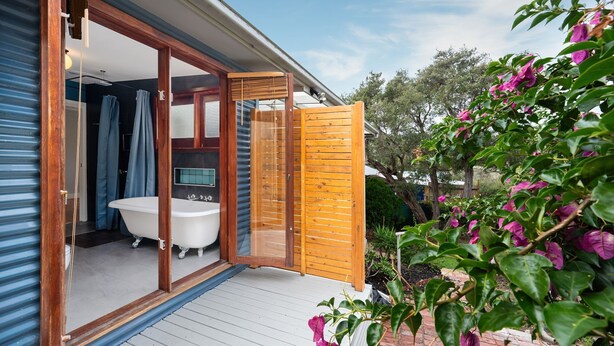 Un baño moderno con una bañera independiente, ducha y puerta de cristal que da a una terraza de madera.