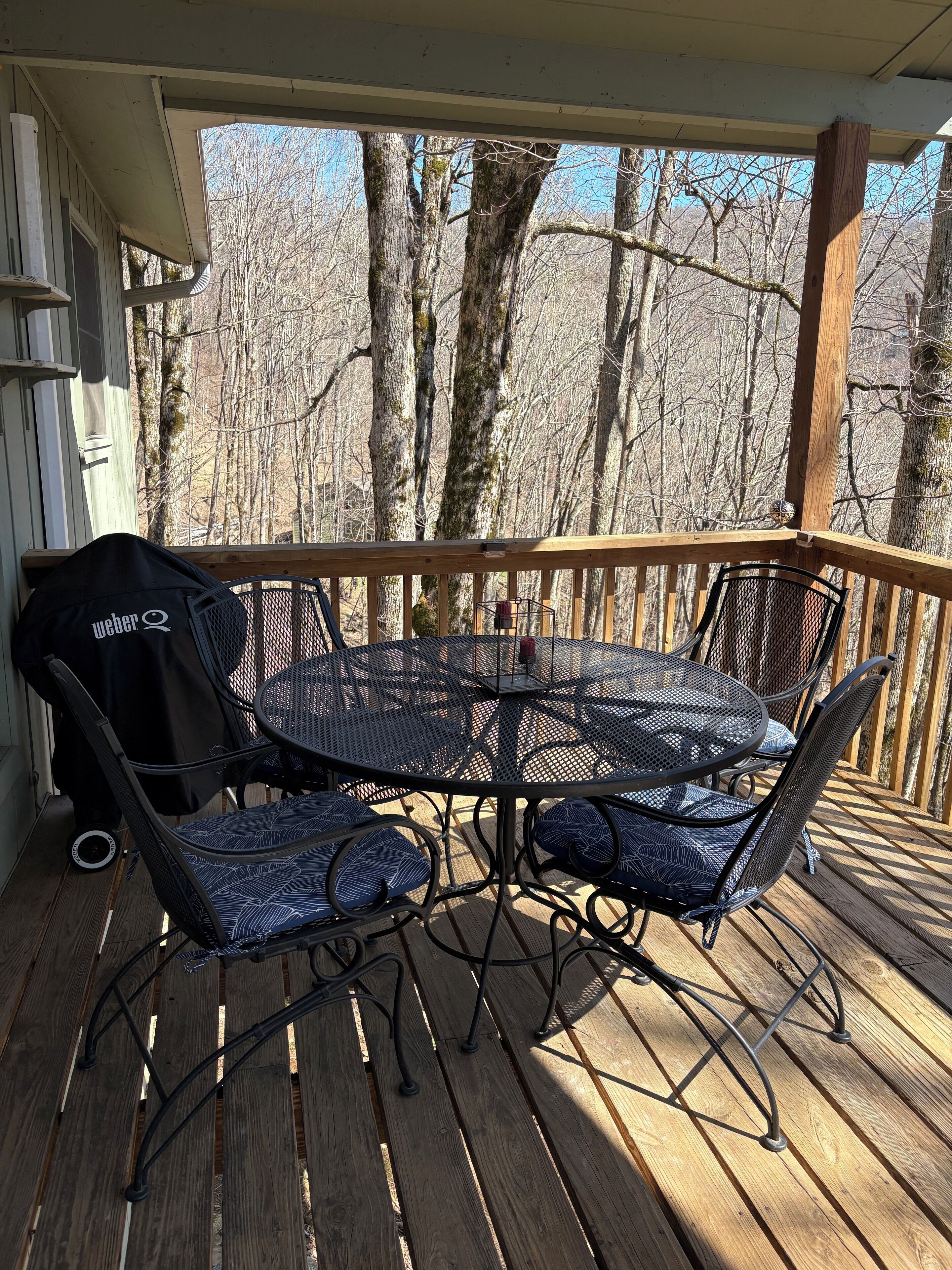 A covered outdoor deck with a round metal table and four chairs, a grill, and a bag labeled "Weber Q" on the left.
