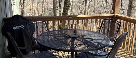 A covered outdoor deck with a round metal table and four chairs, a grill, and a bag labeled "Weber Q" on the left.