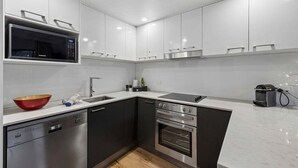A modern kitchen with a dishwasher, oven, microwave, and a red bowl on the counter. - Lantern 07 - Balcony (Thredbo)