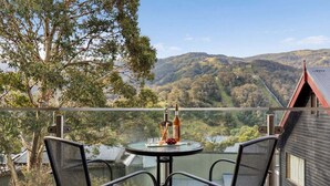 A balcony with two chairs and a table, overlooking a valley with hills and a body of water. - Lantern 07 - Balcony (Thredbo)
