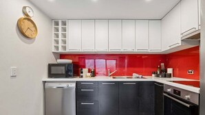Una cocina moderna con armarios blancos, un salpicadero rojo, lavavajillas, microondas y estufa.