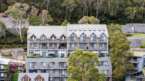 Un hotel de varios pisos con balcones, fachada de piedra y vistas a árboles circundantes.