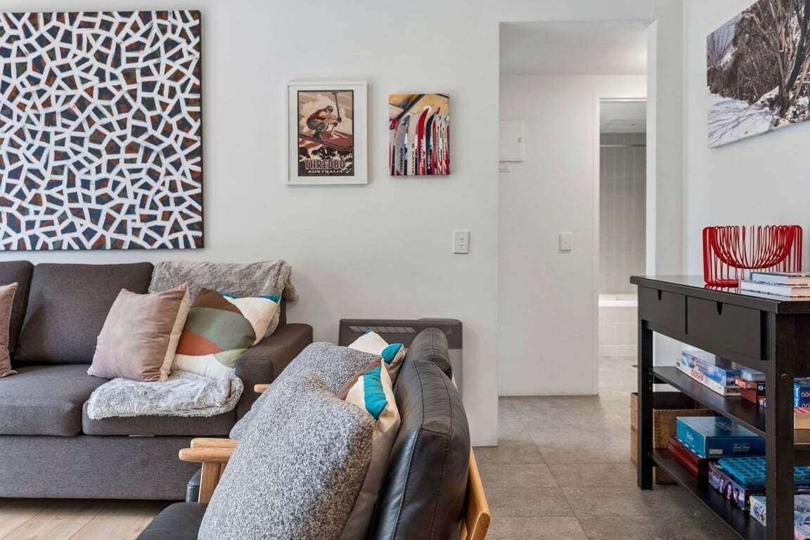 A living room with a sofa, a coffee table, a wall with abstract art, and a bookshelf.
