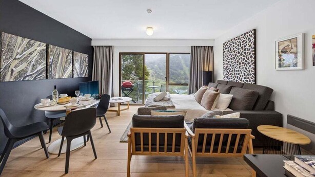 Una sala de estar moderna con sofá, comedor y ventanas grandes.