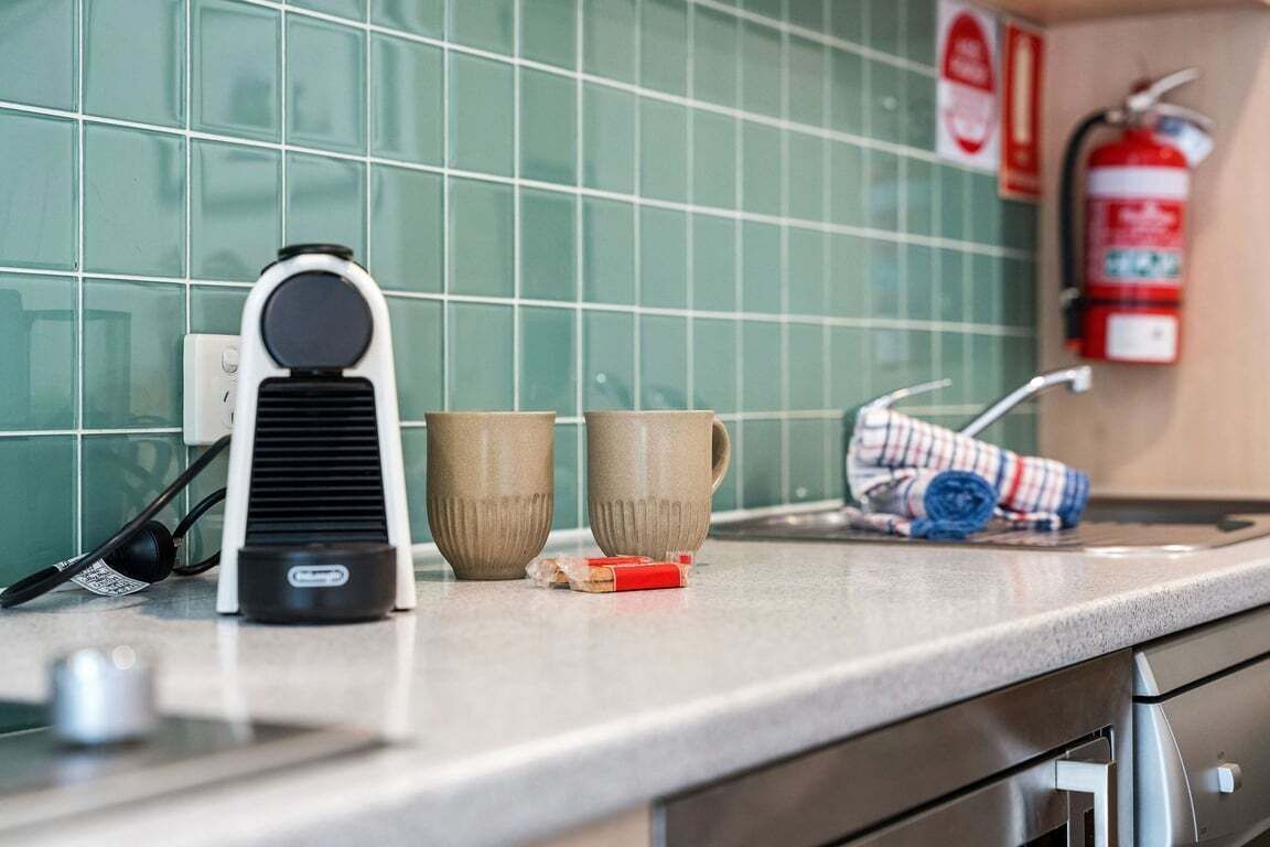 Eine Küchenarbeitsplatte mit Kaffeemaschine, zwei Tassen, einem zusammengerollten Handtuch und einem an der Wand befestigten Feuerlöscher.