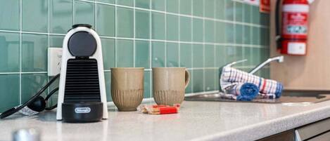 Eine Küchenarbeitsplatte mit Kaffeemaschine, zwei Tassen, einem zusammengerollten Handtuch und einem an der Wand befestigten Feuerlöscher.