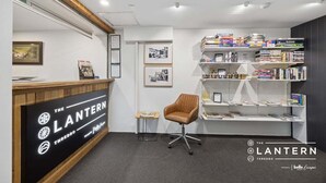 A reception area with a wooden reception desk, a brown office chair, a bookshelf with books, framed pictures on the wall, and a sign that reads 'The Lantern Thredbo.'