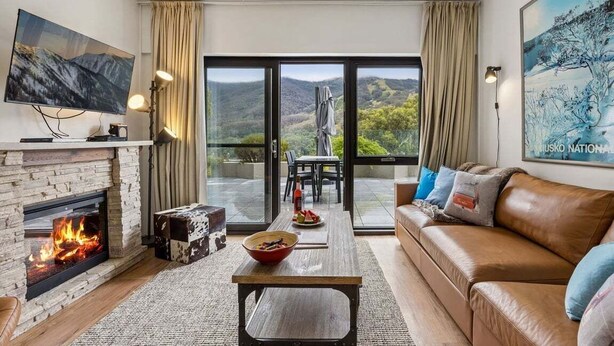 A living room with a fireplace, a sofa, a coffee table, and a TV. There is a balcony with a view of the countryside. - Lantern 14 - Terrace (Thredbo)