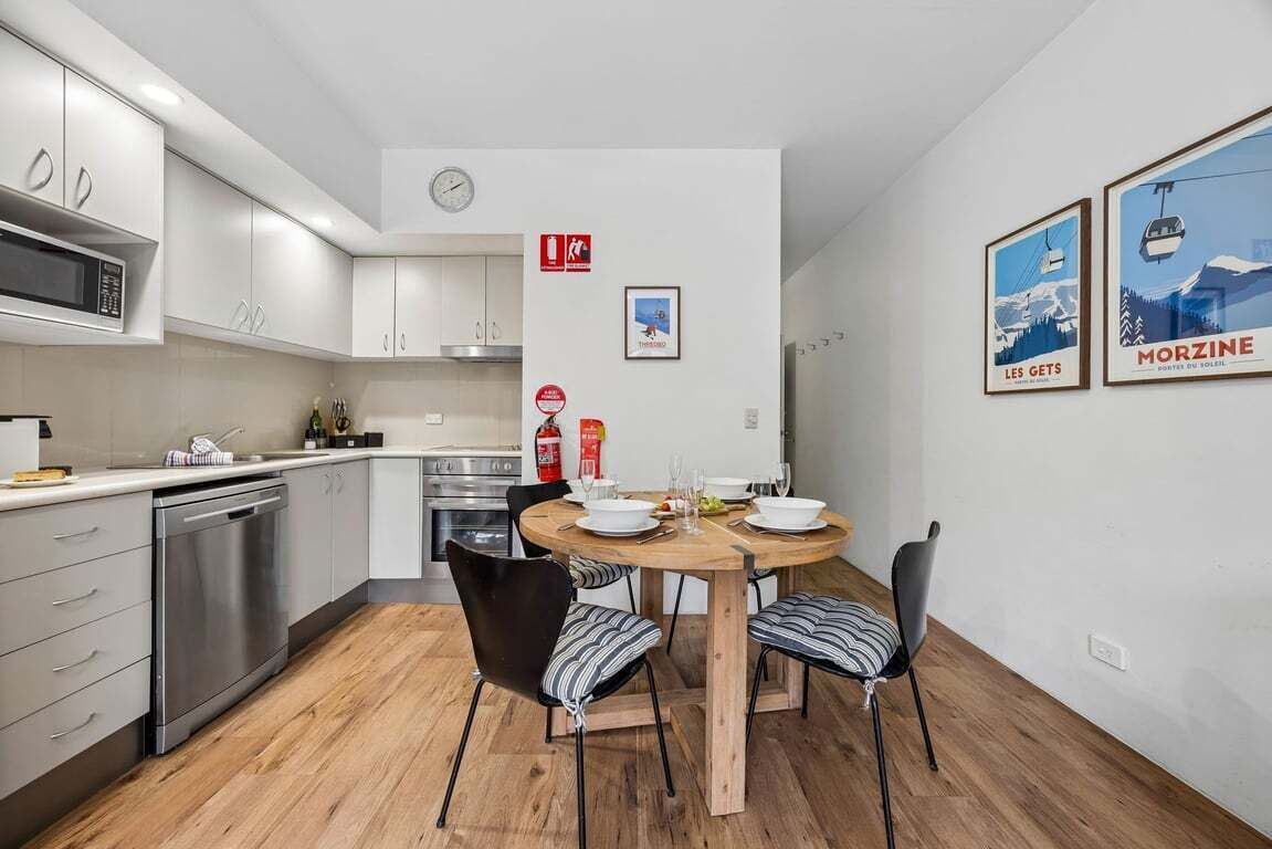 Une cuisine moderne avec des meubles blancs, un four à micro-ondes et un coin repas comprenant une table et des chaises en bois.