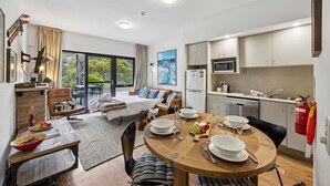 A modern, well-lit room with a dining table set for four, a bed with a view, and a kitchenette. - Lantern 14 - Terrace (Thredbo)