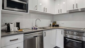 Une cuisine moderne avec des meubles blancs, un four à micro-ondes en acier inoxydable, une machine à café, un évier et un lave-vaisselle.