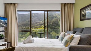 Une chambre d’hôtel équipée d’un lit, d’un canapé, d’une télévision et d’un balcon offrant une vue sur la montagne.