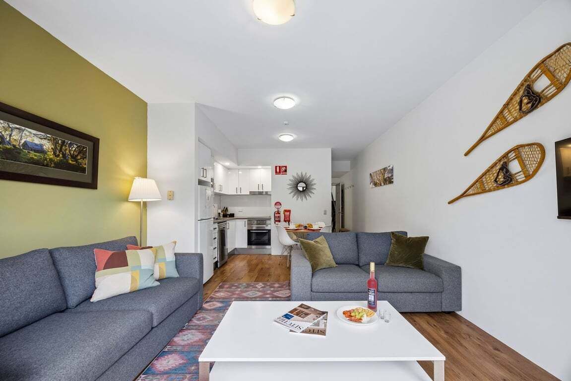 Un salon avec un canapé, une table basse sur laquelle se trouve un magazine, et une cuisine en arrière-plan.