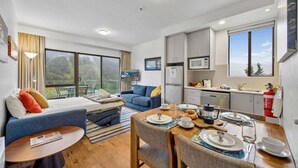 A modern hotel room with a bed, sofa, dining table, and kitchenette. - Lantern 25 - Balcony (Thredbo)