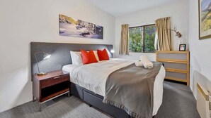 A bedroom with a bed, bedside table, nightstand, window, and artwork on the wall. - Lantern 25 - Balcony (Thredbo)