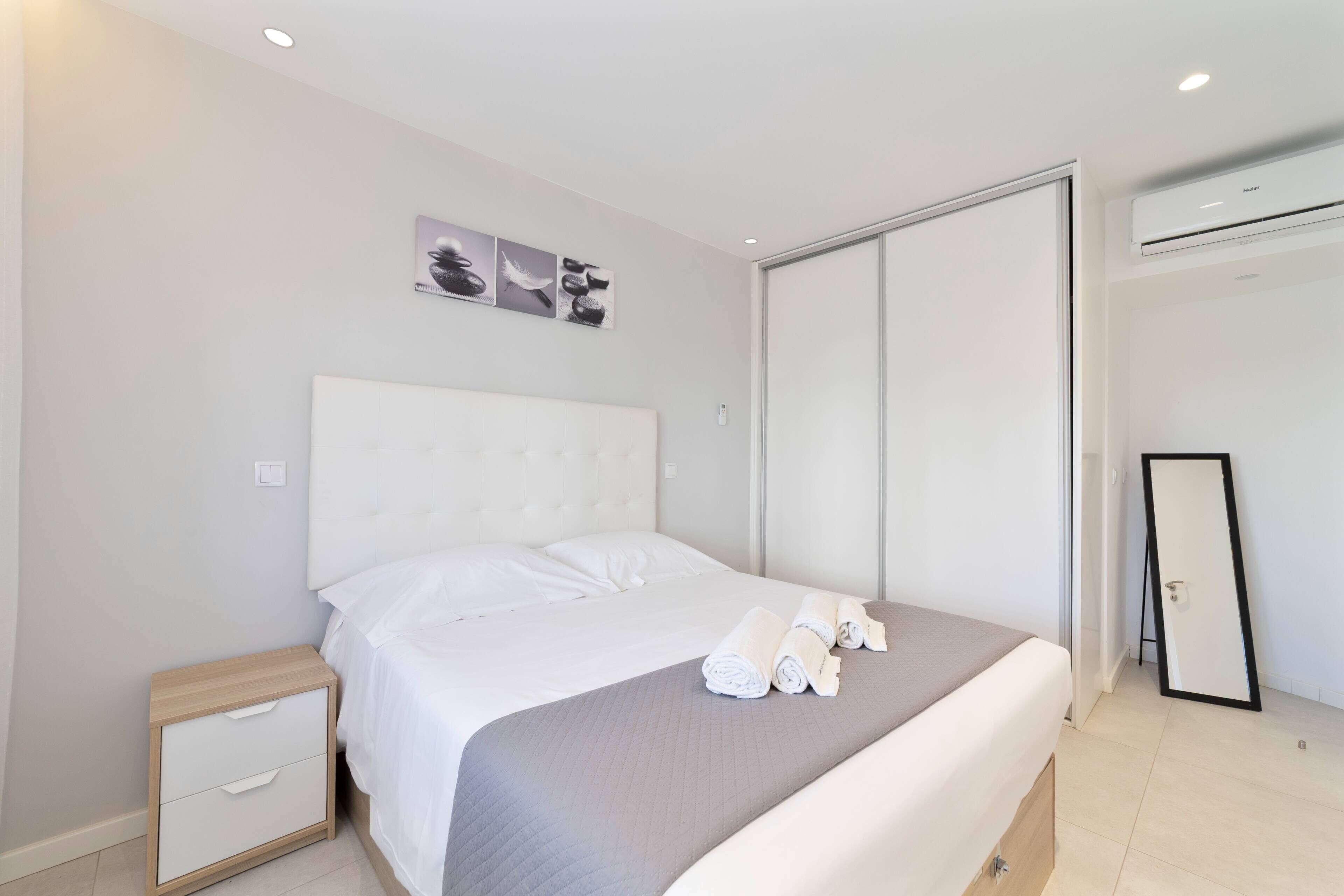 Une chambre d’hôtel moderne équipée d’un grand lit, d’une table de chevet, d’une armoire et d’un appareil de climatisation.