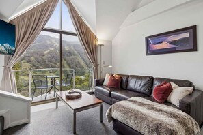 A room with a large window, a leather sofa, a table, and a painting on the wall.