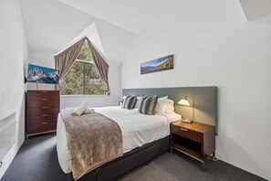 A bedroom with a bed, nightstand, dresser, window, and artwork.