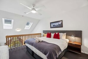 A bedroom with a bed, a nightstand, a desk lamp, a ceiling fan, and a window. - Lantern 28 - 1 bedroom and Loft with 1 carpark (Thredbo)