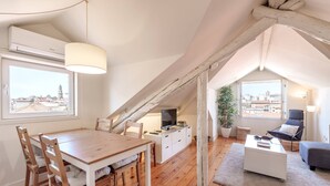 Un appartement-loft chaleureux avec une table à manger en bois, un canapé blanc et un téléviseur posé sur un meuble blanc.