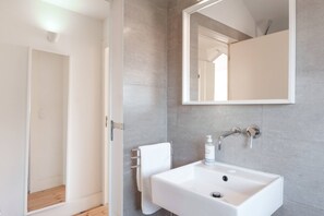 Une salle de bain moderne avec un lavabo blanc, un miroir et un porte-serviettes.