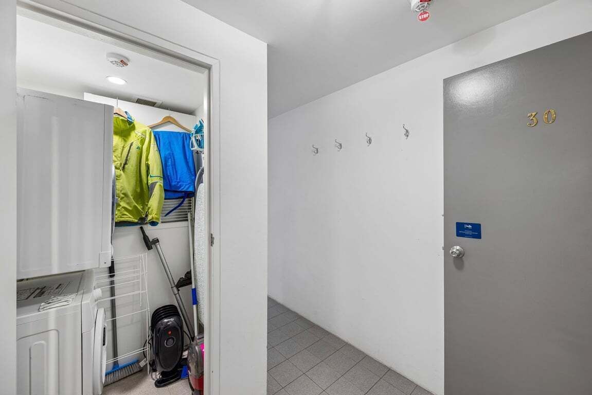 A hotel corridor with a door labeled '30', a coat rack with jackets, and a cleaning cart.