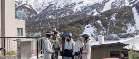 Un grupo de personas con esquíes frente a un edificio con vistas a montañas nevadas.