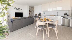 A modern kitchen with white cabinets, a dining table with chairs, and a grey sofa in the living area. - Atlantic Pearl – 5 min to the beach w/ parking (Nazaré)