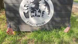Un letrero de madera con un emblema circular que muestra árboles y animales, con la inscripción 'WILDERNESS ADVENTURE'.