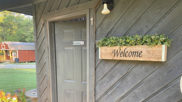Una puerta de madera con un cartel de 'No Fumar', un letrero de bienvenida y una maceta con plantas.