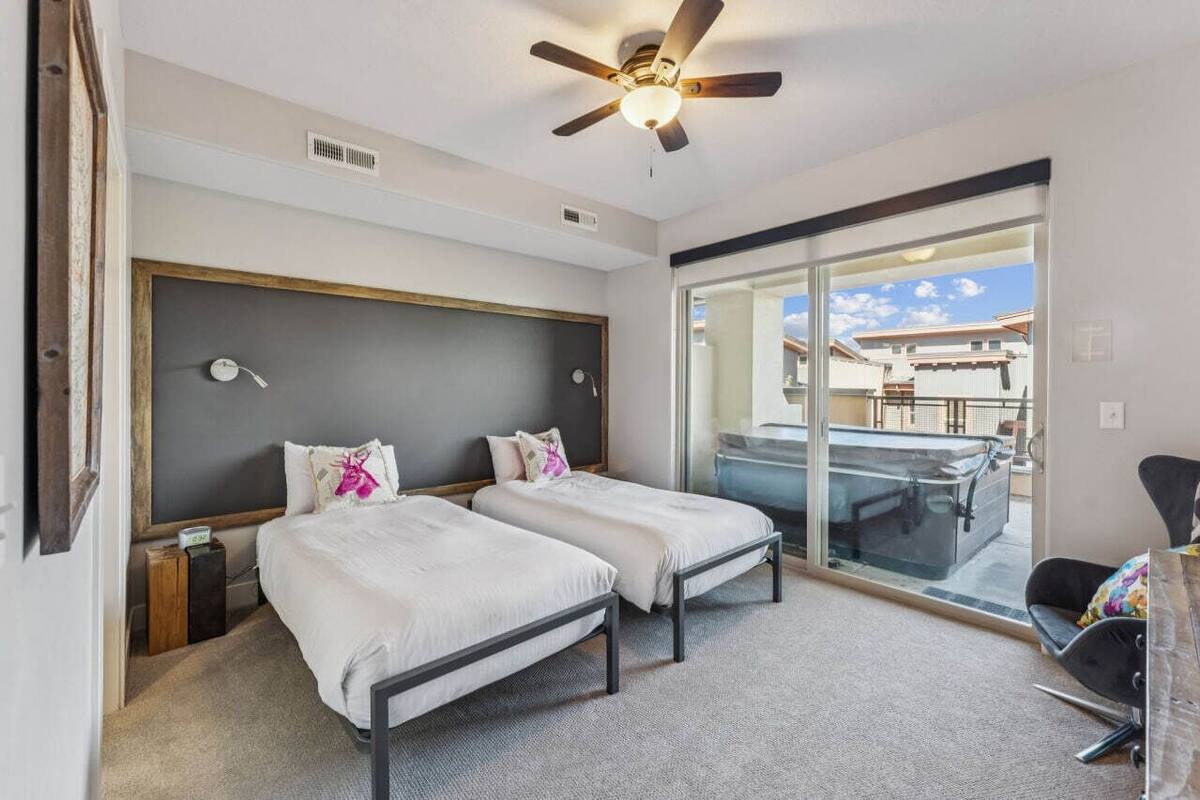 Ein Hotelzimmer mit zwei Betten, einem Deckenventilator, einer großen Schiebetür zum Balkon und Blick ins Freie.