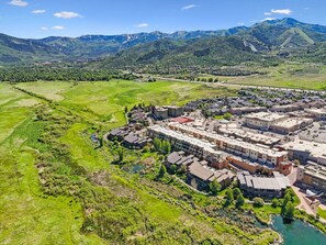 An aerial view of a town with a central cluster of buildings, surrounded by green fields and mountains in the background. - Park Lane South Departments (Park City)