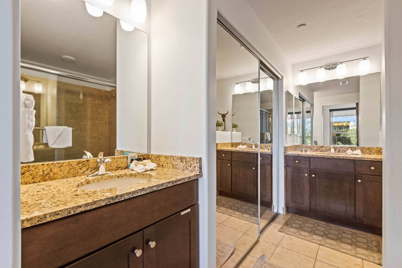A modern bathroom with a granite countertop, a glass shower enclosure, and a large mirror.