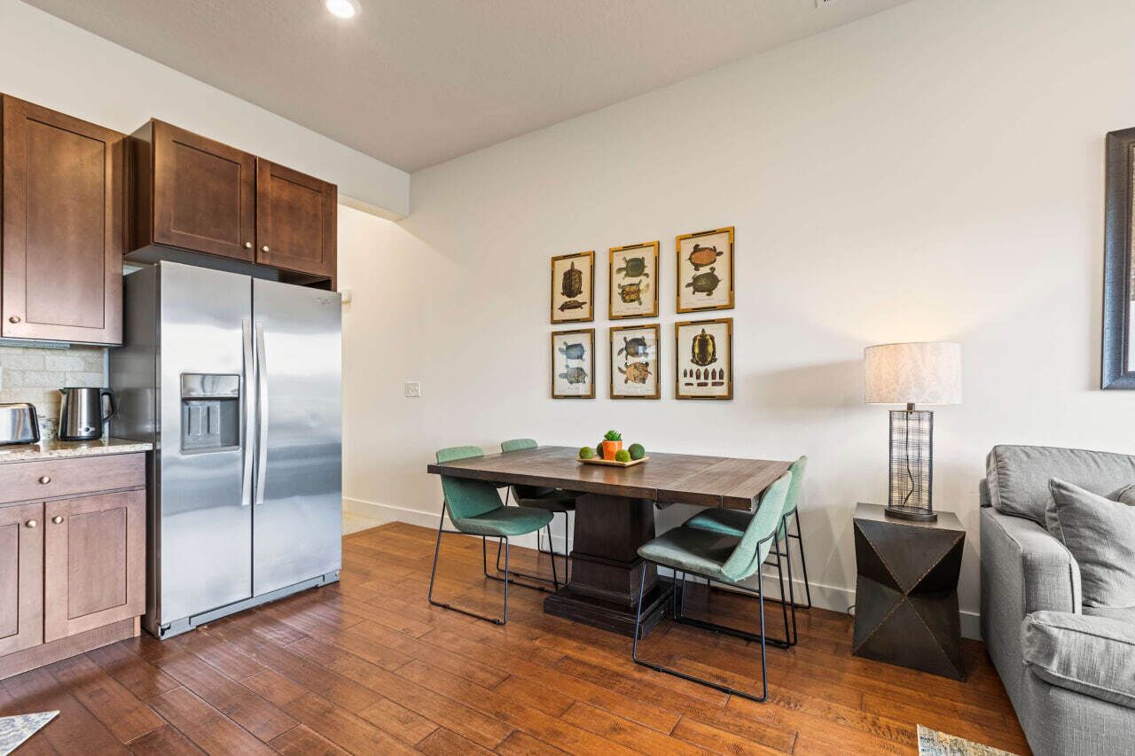 A modern kitchen with a stainless steel refrigerator, wooden cabinets, and a dining area with a dark wooden table and teal chairs.