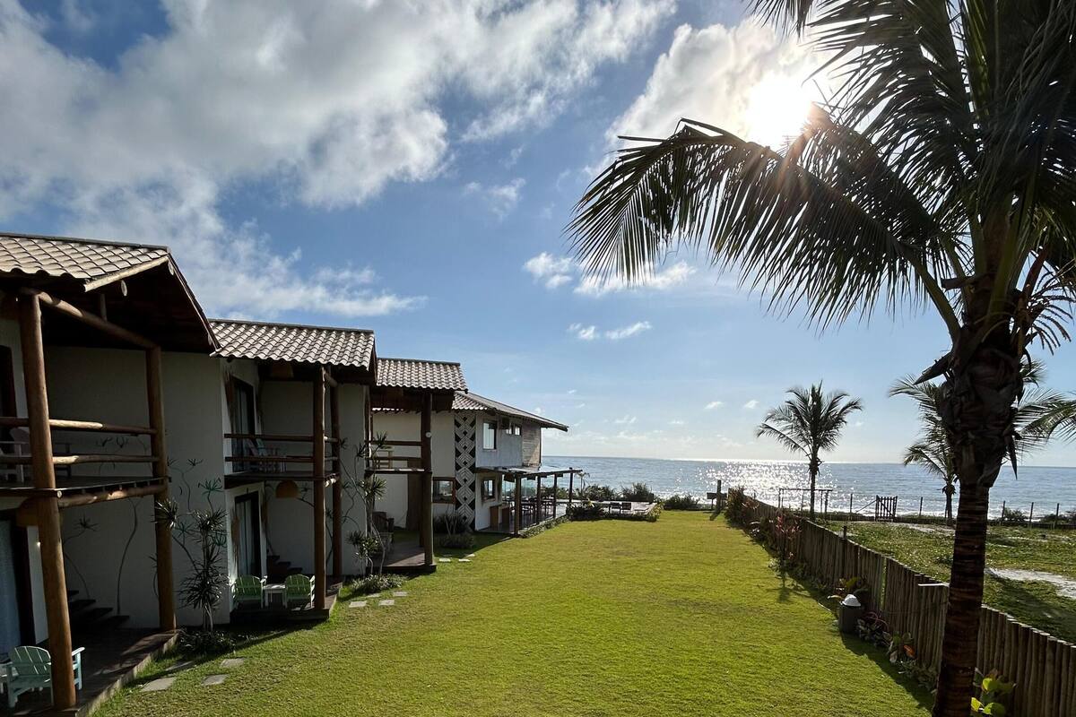 A beachfront property with a well-maintained lawn, a wooden fence, and a view of the ocean.