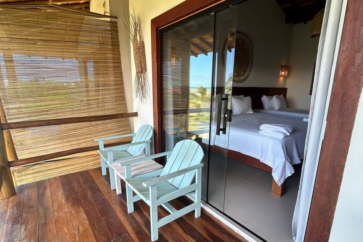 A wooden deck with a glass door leading to a bedroom with a bed and two chairs.