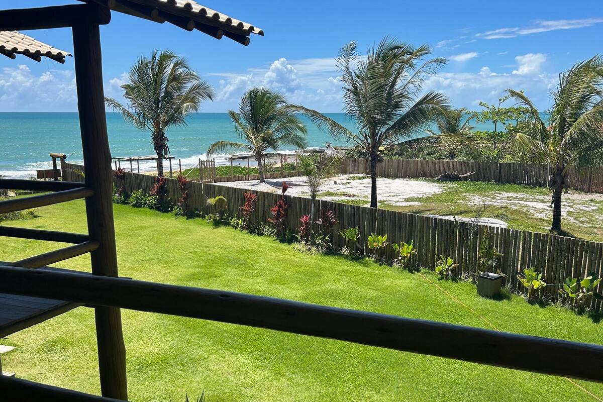 A view from a wooden deck overlooking a beach with palm trees and a sandy area.
