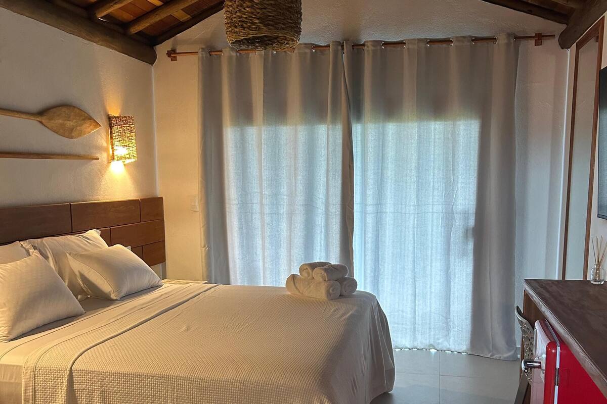 A bedroom with a wooden ceiling, a bed with white bedding, a hanging light fixture, and a red cabinet.