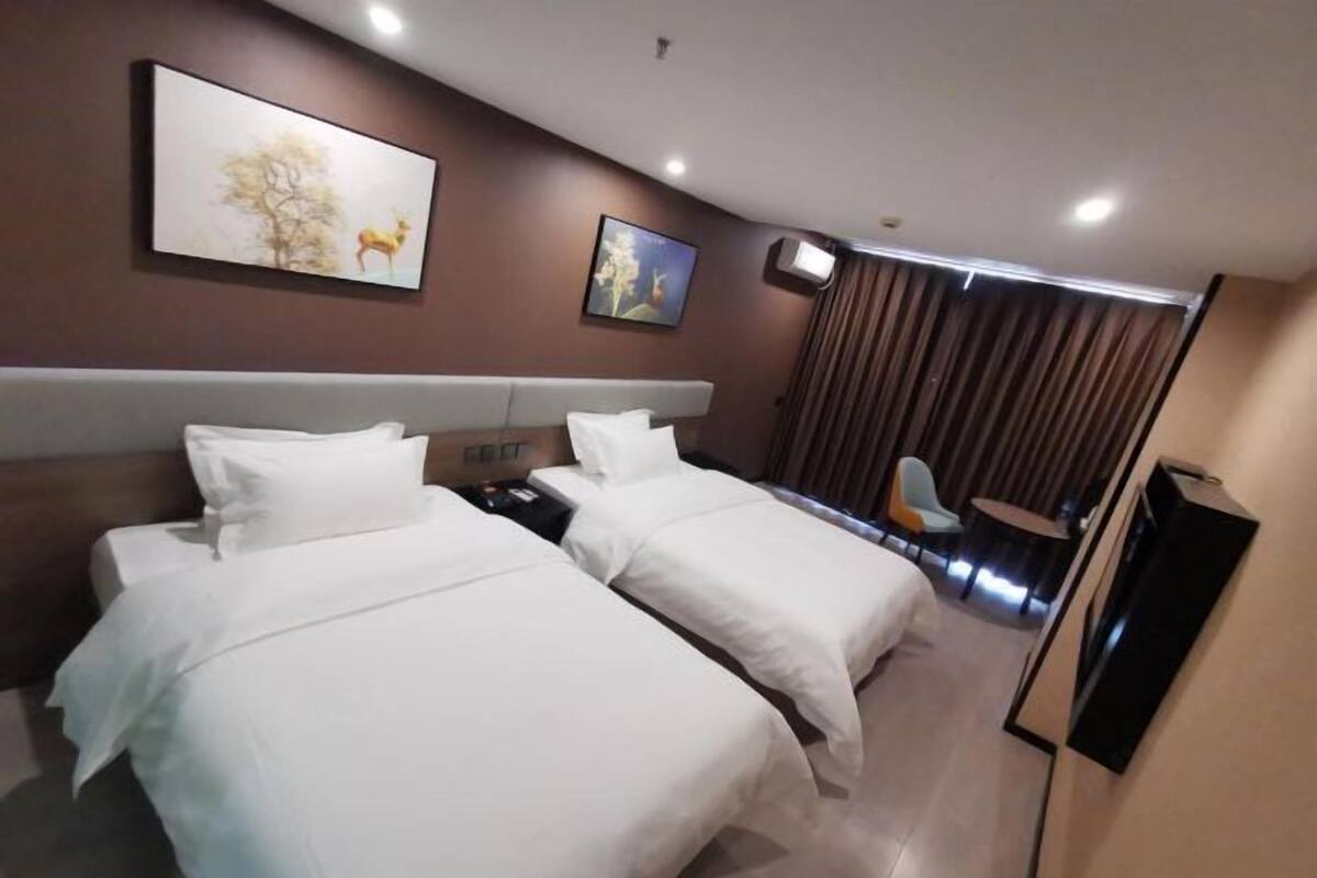 Une chambre d’hôtel avec deux lits, un bureau, une chaise, une télévision et des œuvres d’art accrochées aux murs.